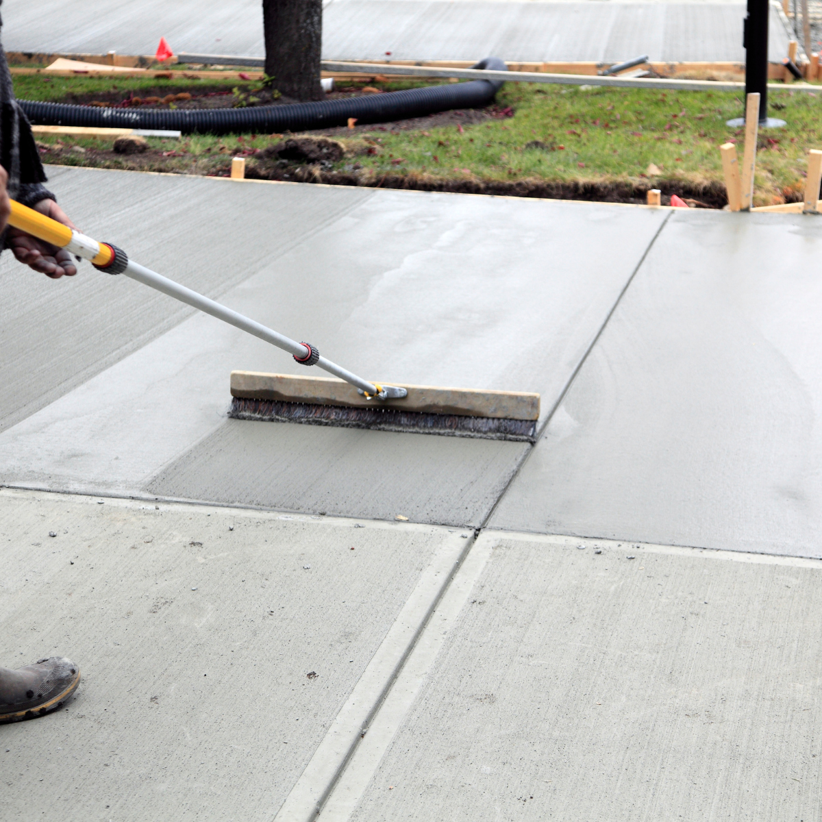 A photo of finishing a freshly poured concrete sidewalk with a broom.